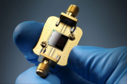 Two fingers in a blue glove hold a golden piece of equipment. 