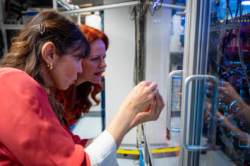 Foto: Land Tirol/Krepper Zwei Frauen blicken durch eine Glasscheibe auf einen Laboraufbau
